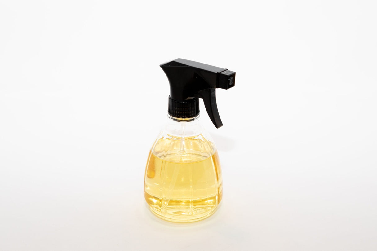 Clear spray bottle with black nozzle containing a yellow liquid on a white background